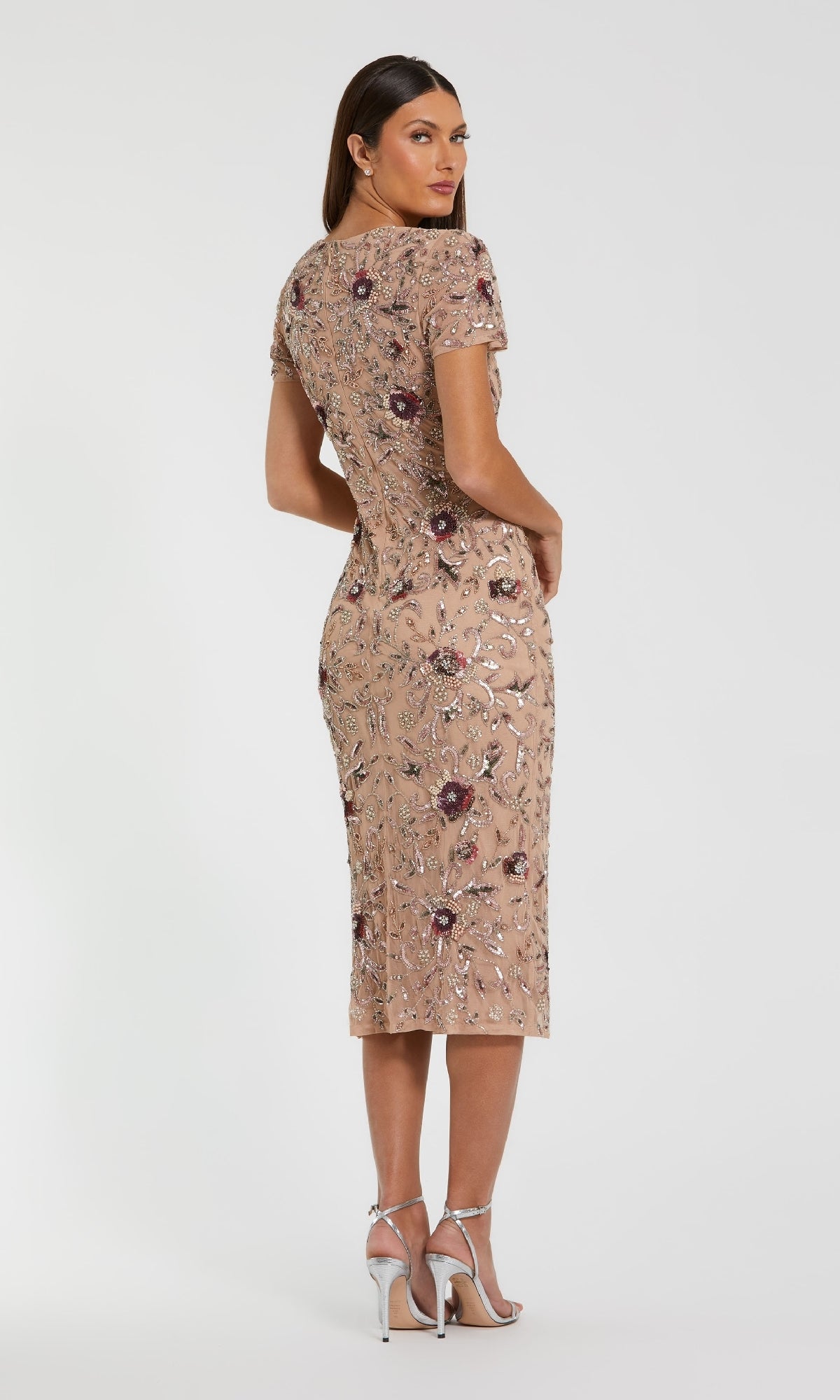 A woman stands in profile wearing the Beaded Midi Wedding Guest Dress: Mac Duggal 10102, a nude midi dress with floral sequin embroidery, styled with silver high-heeled sandals against a plain white background.